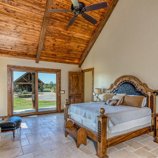 Diseño de dormitorio principal, rural, grande, con paredes beige, suelo de travertino, estufa de leña, marco de chimenea de piedra y suelo beige