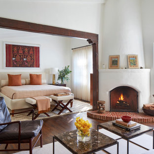 Cette image montre une chambre parentale méditerranéenne avec un mur blanc, une cheminée d'angle, un manteau de cheminée en plâtre, un sol marron et un sol en bois foncé.
