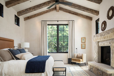 Bedroom - large mediterranean master light wood floor and beige floor bedroom idea in Orange County with beige walls, a standard fireplace and a stone fireplace