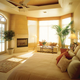 Diseño de dormitorio principal, mediterráneo, grande, con paredes beige, moqueta, chimenea tradicional y marco de chimenea de piedra