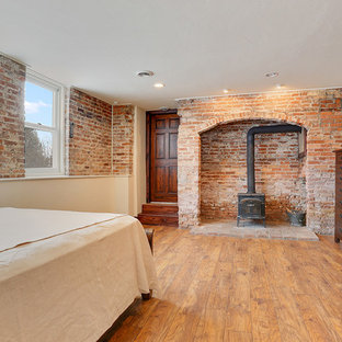 Foto de habitación de invitados rural, grande, con paredes blancas, suelo de madera en tonos medios, estufa de leña y marco de chimenea de ladrillo