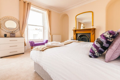 Large classic master bedroom in Devon with beige walls, carpet, a wooden fireplace surround and beige floors.