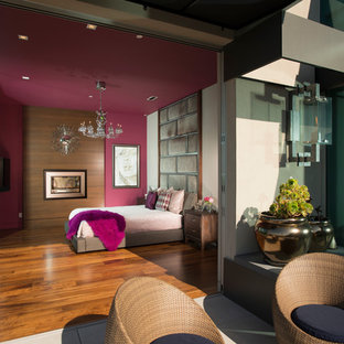 Modelo de dormitorio principal, moderno, grande, sin chimenea, con paredes multicolor, suelo de madera en tonos medios y marco de chimenea de madera