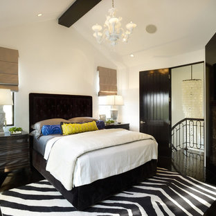 Mediterranean bedroom in Los Angeles with white walls, a corner fireplace, a stone fireplace surround and black floors.