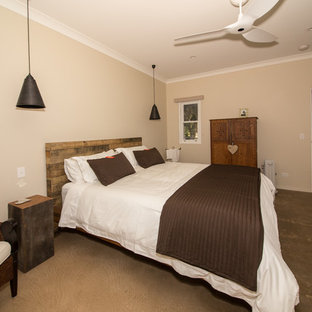 Ejemplo de dormitorio principal, de estilo de casa de campo, de tamaño medio, con paredes beige, suelo de cemento, marco de chimenea de piedra y estufa de leña