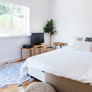 Beach style guest bedroom in Melbourne with white walls, medium hardwood floors and brown floor.