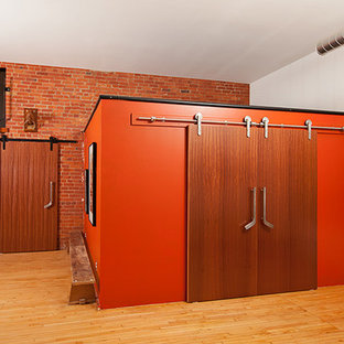 Ejemplo de dormitorio tipo loft, industrial, de tamaño medio, con suelo de madera clara y parades naranjas