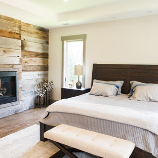 Foto de dormitorio principal, rural, grande, con paredes beige, suelo de madera oscura, chimenea de doble cara, marco de chimenea de madera y suelo marrón