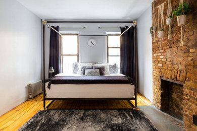 ニューヨークにある小さなエクレクティックスタイルのおしゃれな主寝室 (グレーの壁、無垢フローリング、標準型暖炉、レンガの暖炉まわり) のインテリア