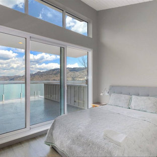 Design ideas for a mid-sized beach style master bedroom in Vancouver with grey walls, vinyl floors, grey floor, timber, a hanging fireplace and a plaster fireplace surround.