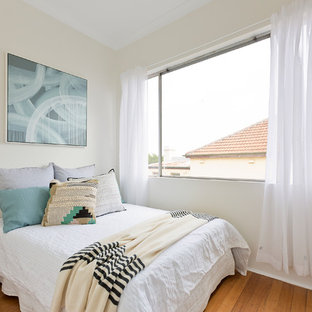 Design ideas for a mid-sized transitional guest bedroom in Sydney with medium hardwood floors, beige walls and brown floor.