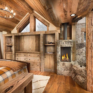 Imagen de dormitorio principal, rústico, grande, con paredes beige, suelo de madera en tonos medios, estufa de leña y marco de chimenea de piedra