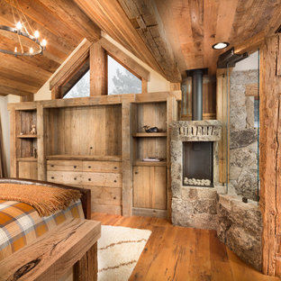 Mittelgroßes Uriges Hauptschlafzimmer mit beiger Wandfarbe, braunem Holzboden, Kaminumrandung aus Stein, Kaminofen und orangem Boden in Sacramento