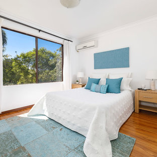 Beach style guest bedroom in Sydney with white walls, medium hardwood floors and brown floor.