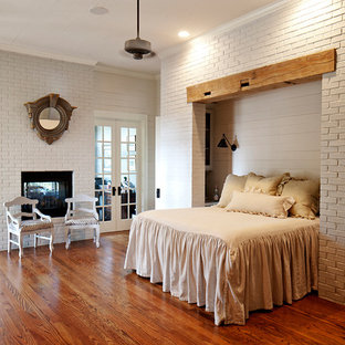 Modelo de dormitorio de estilo de casa de campo con paredes grises, suelo de madera oscura, chimenea de doble cara y marco de chimenea de ladrillo