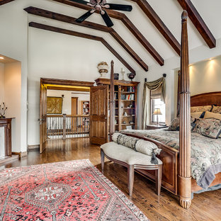 Modelo de dormitorio principal, clásico, grande, con paredes beige, suelo de madera en tonos medios, chimenea tradicional, marco de chimenea de madera y suelo marrón