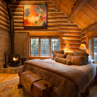 Diseño de dormitorio principal, rústico, grande, con suelo de madera clara, estufa de leña y marco de chimenea de ladrillo