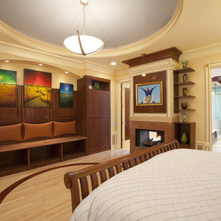 Ejemplo de dormitorio principal, bohemio, grande, con suelo de madera clara, chimenea de doble cara y marco de chimenea de piedra