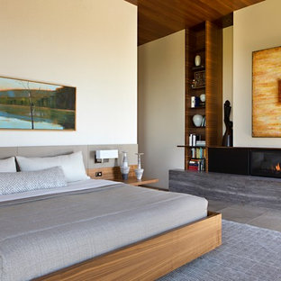 Ejemplo de dormitorio principal, actual, grande, con paredes beige, chimenea lineal, suelo gris, suelo de piedra caliza y marco de chimenea de piedra
