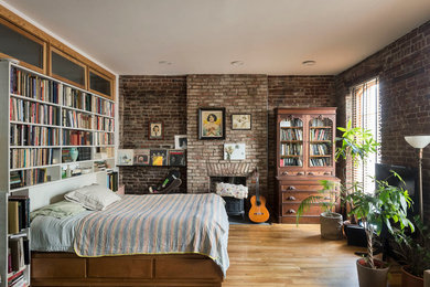 ニューヨークにある小さなインダストリアルスタイルのおしゃれな寝室 (淡色無垢フローリング、薪ストーブ、レンガの暖炉まわり)