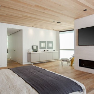 Imagen de dormitorio principal, ecléctico, grande, con paredes blancas, suelo de bambú, chimenea lineal, marco de chimenea de yeso y suelo beige