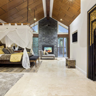 Foto de dormitorio principal, exótico, extra grande, con chimenea de doble cara, marco de chimenea de piedra y suelo multicolor