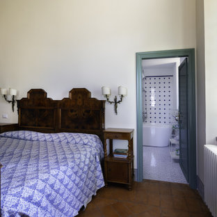 Foto de dormitorio principal, clásico, extra grande, con paredes blancas, suelo de ladrillo, chimenea tradicional, marco de chimenea de piedra y suelo marrón