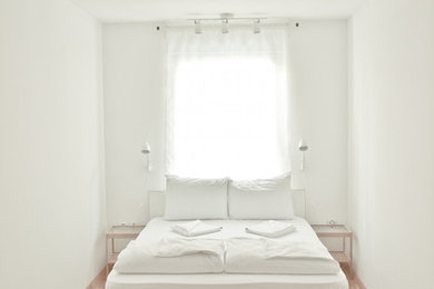 Bild på ett stort medelhavsstil sovrum, med vita väggar och mellanmörkt trägolv