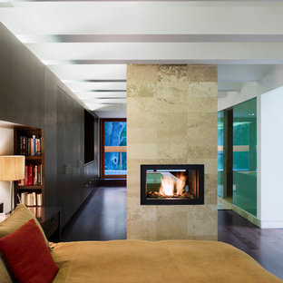 Diseño de dormitorio principal, moderno, pequeño, con paredes negras, suelo de madera oscura, chimenea de doble cara y marco de chimenea de piedra