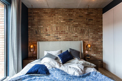 Photo of an industrial grey and brown bedroom in London with blue walls, light hardwood flooring and brown floors.
