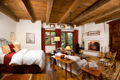 Foto de habitación de invitados mediterránea grande con paredes blancas, suelo de madera en tonos medios, todas las chimeneas y marco de chimenea de yeso