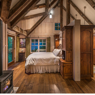 Diseño de dormitorio principal, de estilo de casa de campo, grande, con paredes beige, suelo de madera en tonos medios y estufa de leña