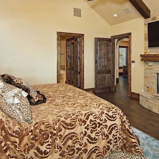 Idee per una grande camera matrimoniale rustica con pareti beige, pavimento in legno massello medio, camino sospeso e cornice del camino in pietra