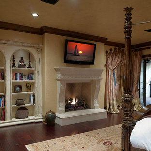 Modelo de dormitorio principal, mediterráneo, grande, con paredes beige, suelo de madera oscura, chimenea tradicional y marco de chimenea de hormigón