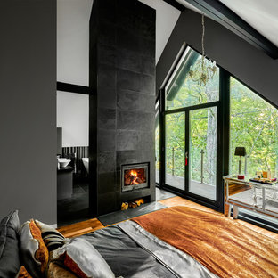 Modelo de dormitorio principal, escandinavo, de tamaño medio, con paredes grises, suelo de madera clara, estufa de leña, marco de chimenea de baldosas y/o azulejos y suelo marrón