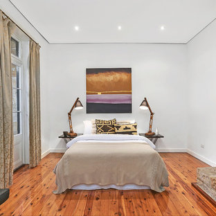 This is an example of a transitional bedroom in Sydney with white walls, medium hardwood floors, a standard fireplace, a stone fireplace surround and brown floor.