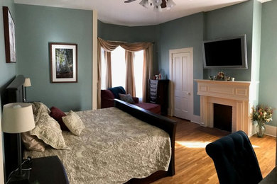 クリーブランドにある巨大なトランジショナルスタイルのおしゃれな主寝室 (緑の壁、無垢フローリング、標準型暖炉、木材の暖炉まわり、茶色い床)