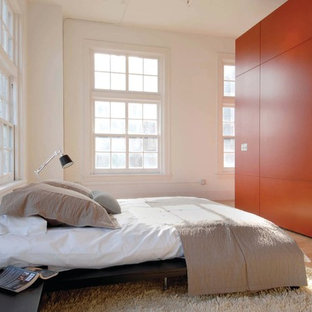 Imagen de dormitorio tipo loft, minimalista, con parades naranjas y suelo de madera clara