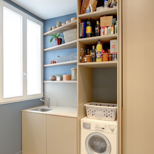 Idée de décoration pour une buanderie linéaire design multi-usage et de taille moyenne avec un évier encastré, des portes de placard beiges, un mur bleu et un sol en carrelage de céramique.