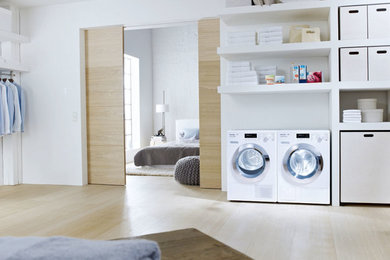 Einzeilige, Große Moderne Waschküche mit weißen Schränken, weißer Wandfarbe, hellem Holzboden und Waschmaschine und Trockner nebeneinander in Oxfordshire