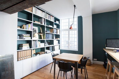 Modelo de despacho contemporáneo de tamaño medio con biblioteca, paredes azules, suelo de madera clara y escritorio empotrado