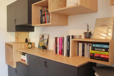 Diseño de despacho actual de tamaño medio con biblioteca, paredes blancas, suelo de madera oscura, chimenea de esquina, marco de chimenea de yeso, escritorio independiente y suelo marrón