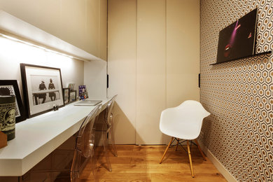 Imagen de despacho actual pequeño sin chimenea con biblioteca, paredes multicolor, suelo de madera en tonos medios, escritorio empotrado y suelo marrón