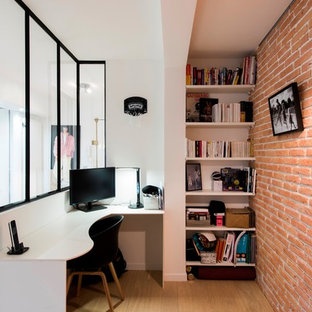 Aménagement d'un petit bureau industriel avec un mur blanc, un sol en bois brun, un bureau intégré et un sol marron.