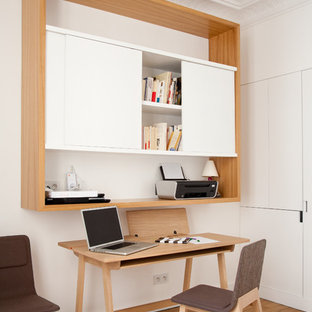 Foto på ett litet funkis hemmabibliotek, med vita väggar, mellanmörkt trägolv och ett fristående skrivbord