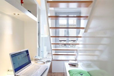 This is an example of a small contemporary study in Paris with white walls, light hardwood flooring, a built-in desk, no fireplace and brown floors.