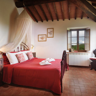 Modelo de dormitorio principal, de estilo de casa de campo, de tamaño medio, con paredes blancas, suelo de baldosas de terracota y suelo naranja