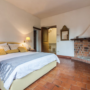 Esempio di una camera matrimoniale classica con camino ad angolo, pareti bianche, pavimento in terracotta, cornice del camino in mattoni e pavimento marrone
