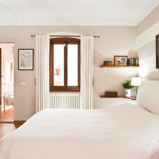 Modelo de dormitorio principal, romántico, pequeño, con paredes blancas, suelo de madera clara, chimenea tradicional, marco de chimenea de piedra y suelo marrón
