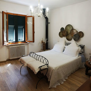 Modelo de dormitorio principal, urbano, grande, con paredes blancas, suelo de madera clara, chimenea lineal, marco de chimenea de ladrillo y suelo marrón